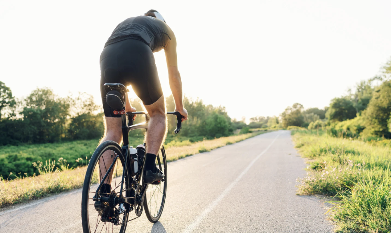 Cyclist riding on an open road surrounded by greenery, promoting outdoor exercise for mental and cardiovascular health.