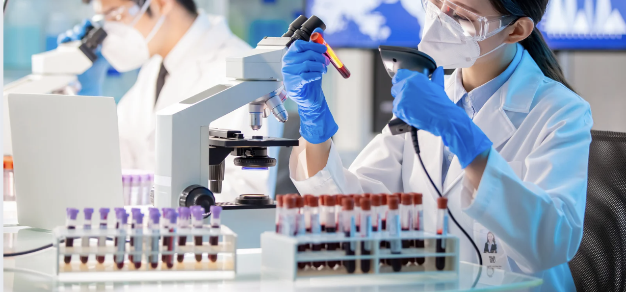 Scientist in a laboratory scanning a blood sample vial while wearing protective gear, conducting biomedical research and diagnostics.