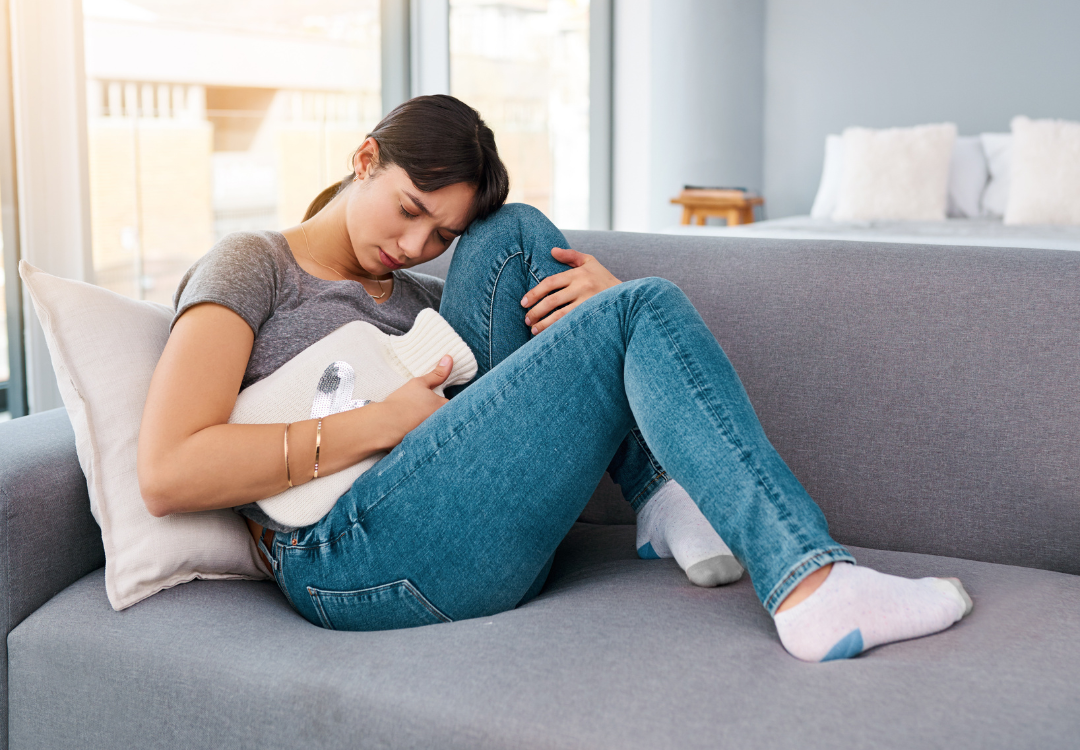 Teenage girl sitting on couch curled up and in pain, possibly due to PMS.